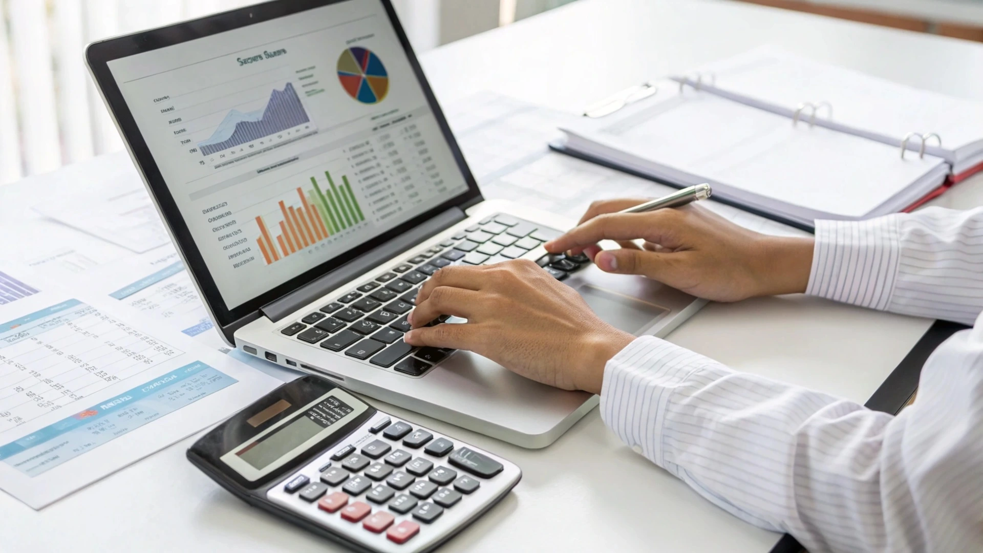 Person typing on a macbook with a calculator at their side demonstrating bookkeeping services