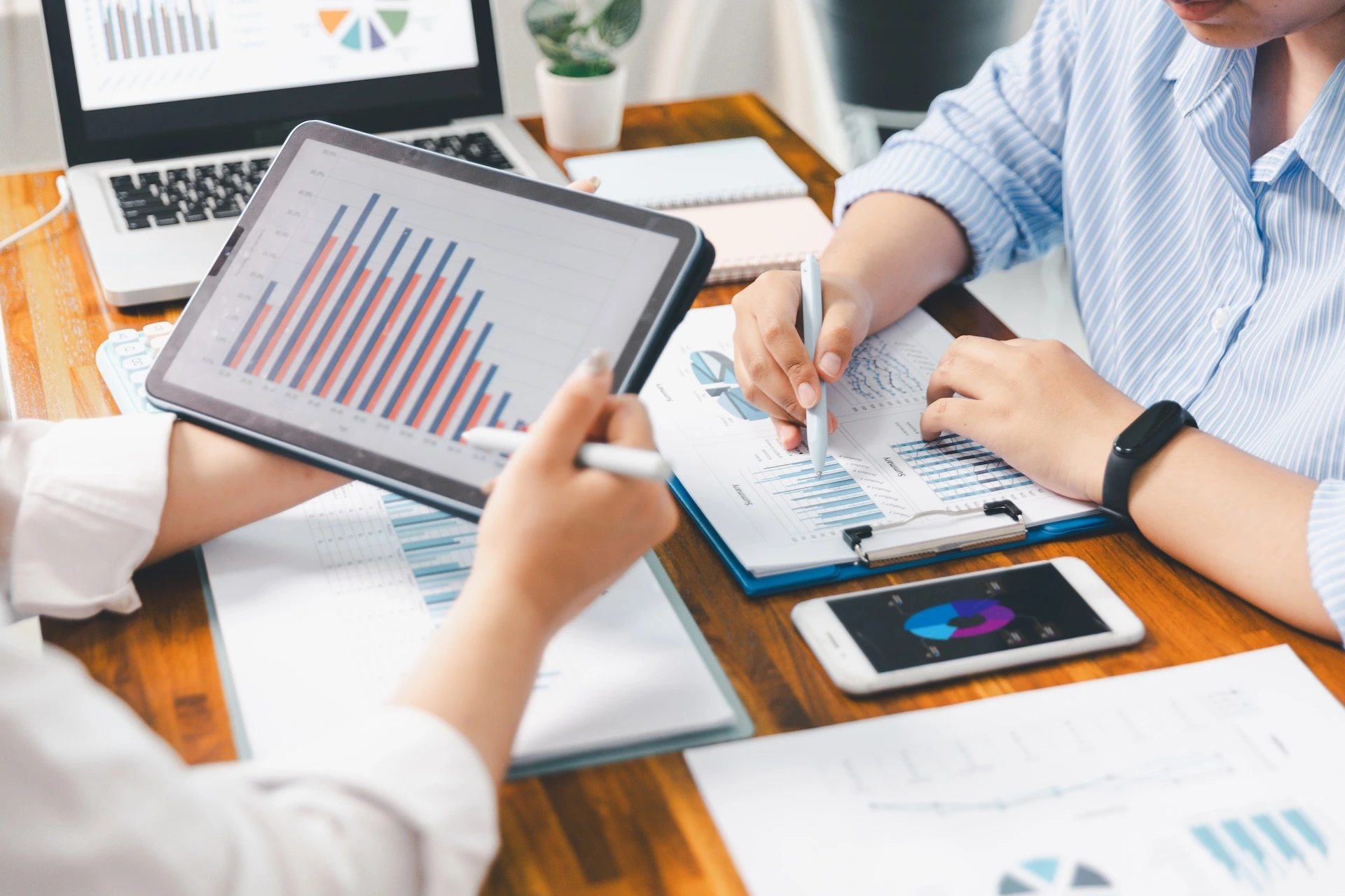 Two accountants looking at charts and tables on paper and mobile devices performing personal tax services
