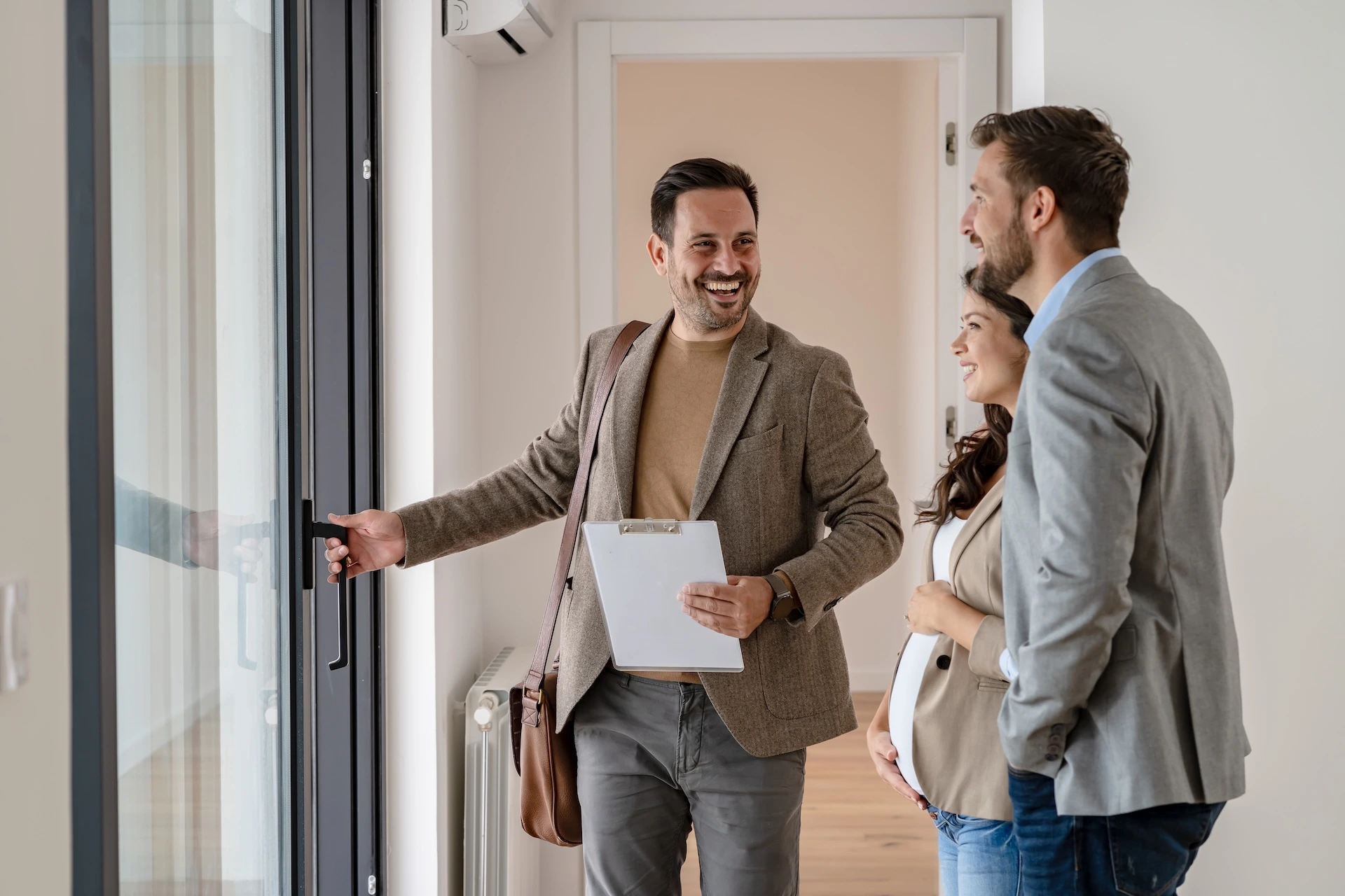 Estate agent with a clipboard showing a young couple around a home