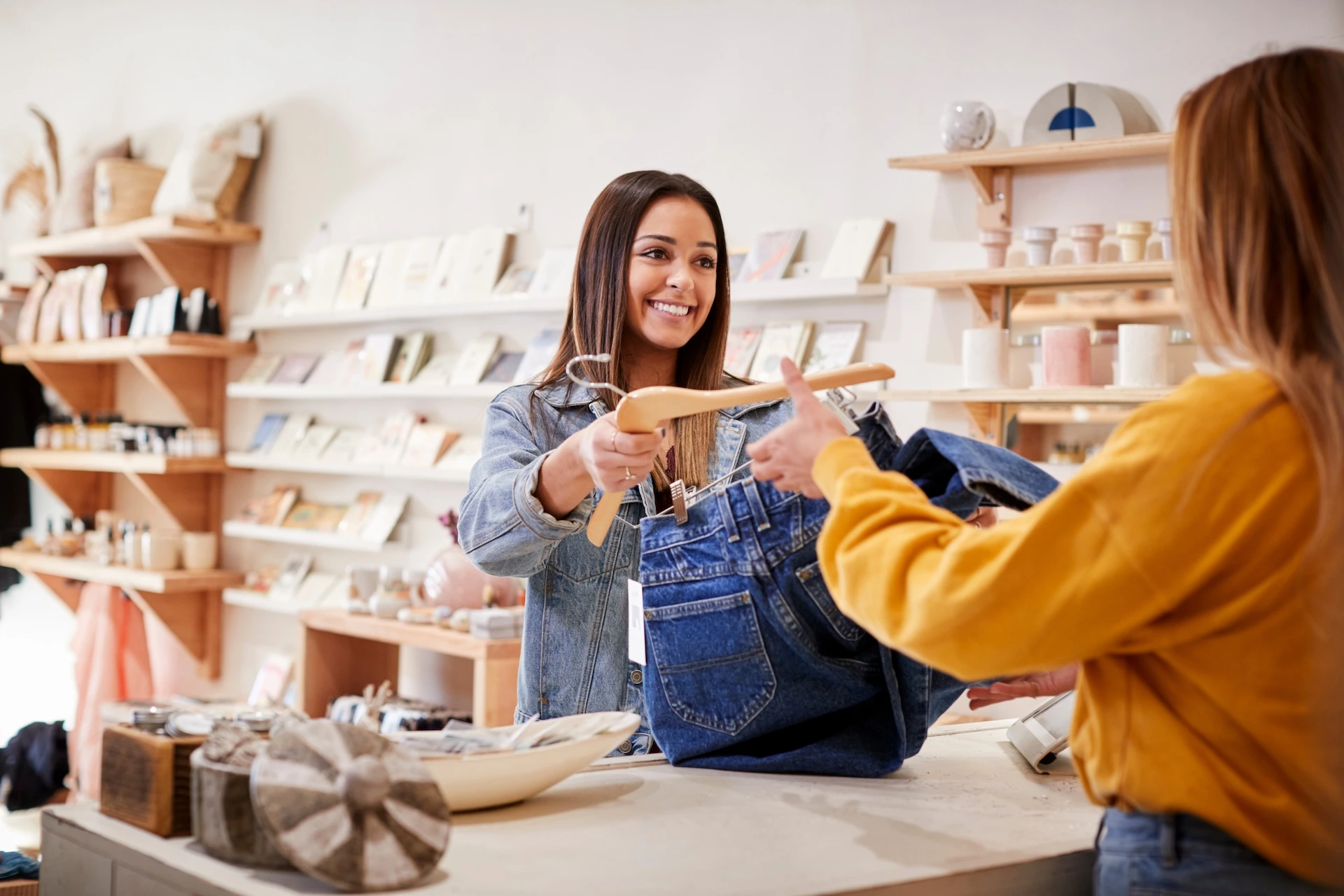 Woman handing a pair of jeans to a cashier ready for purchase