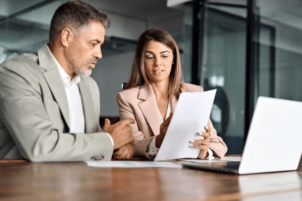 Man and woman sitting in front of a laptop reviewing some paperwork